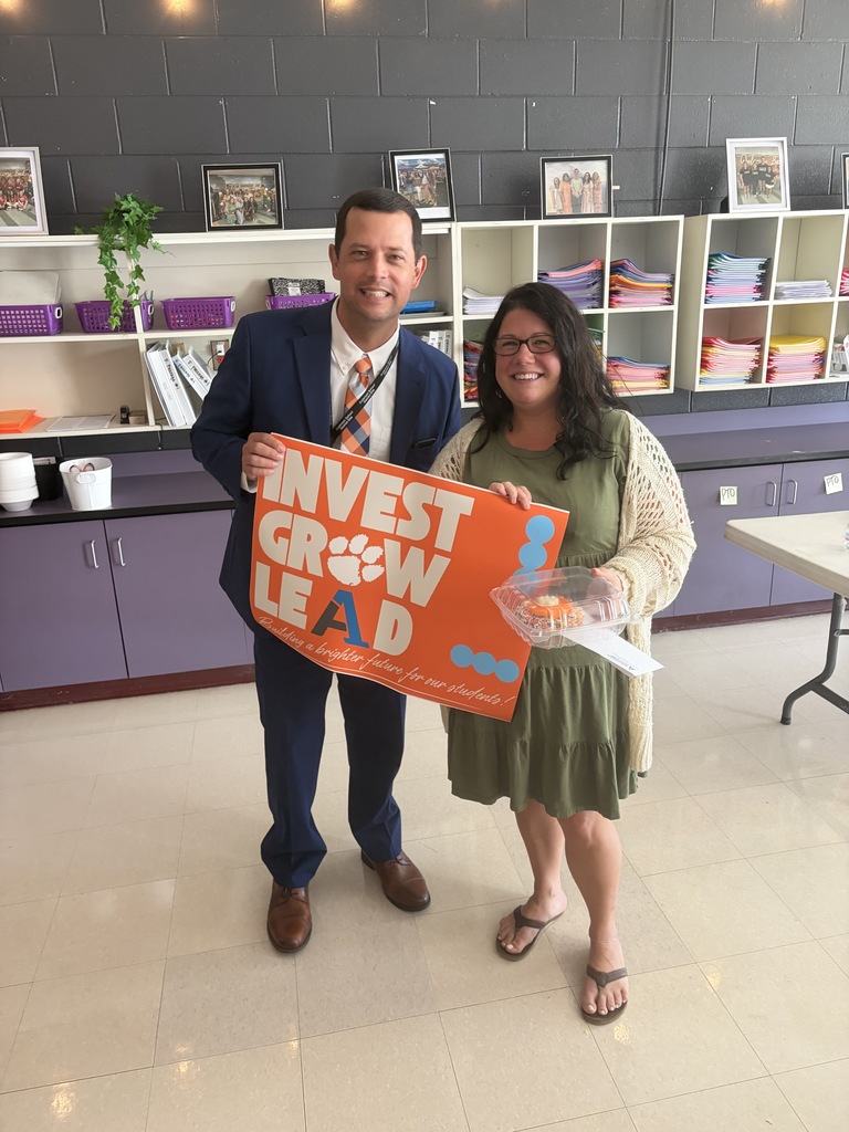 A staff member poses for a picture with an educator with a sign that says Invest Grow Lead - Building a better future for our students