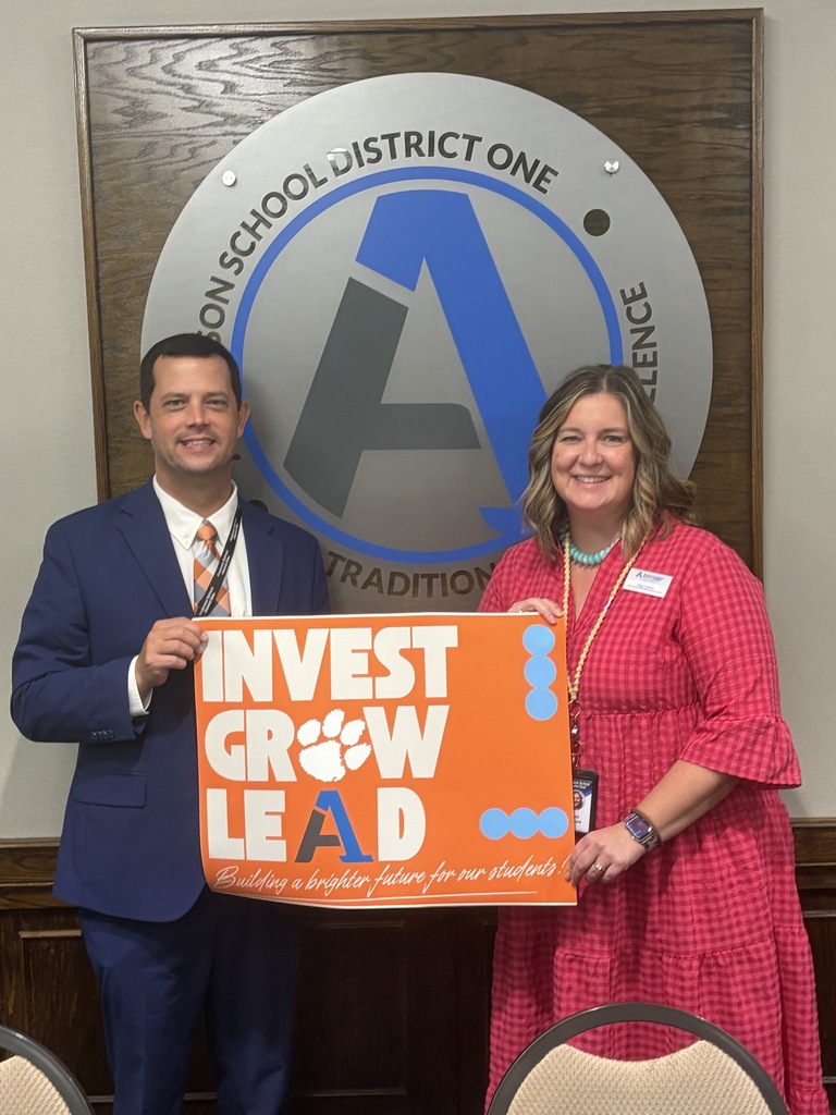 A staff member poses for a picture with an educator with a sign that says Invest Grow Lead - Building a better future for our students