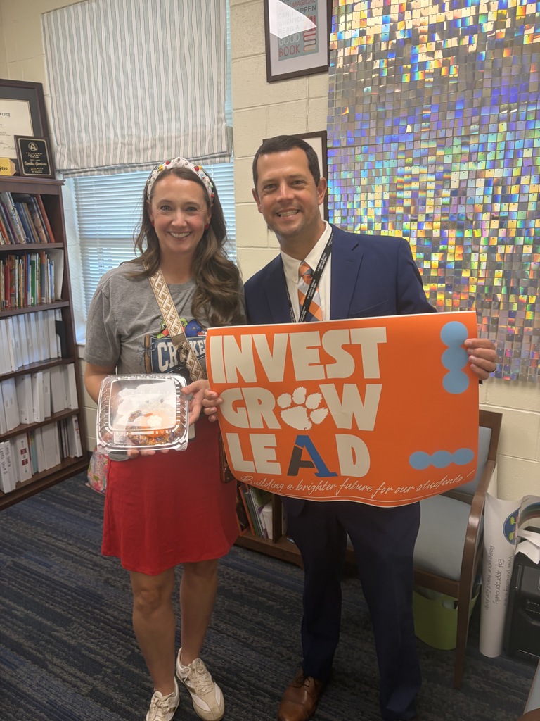 A staff member poses for a picture with an educator with a sign that says Invest Grow Lead - Building a better future for our students