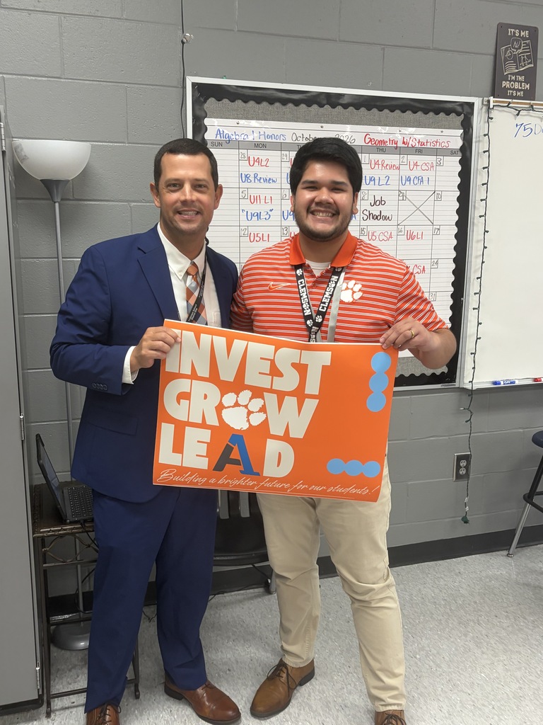 A staff member poses for a picture with an educator with a sign that says Invest Grow Lead - Building a better future for our students