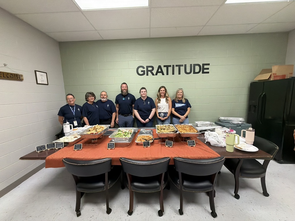 Midway Bible Church volunteers and Spearman staff stand behind a table filled with a catered lunch, served to teachers and staff in celebration of finishing the first nine weeks strong. The word “GRATITUDE” is displayed on the wall behind them.