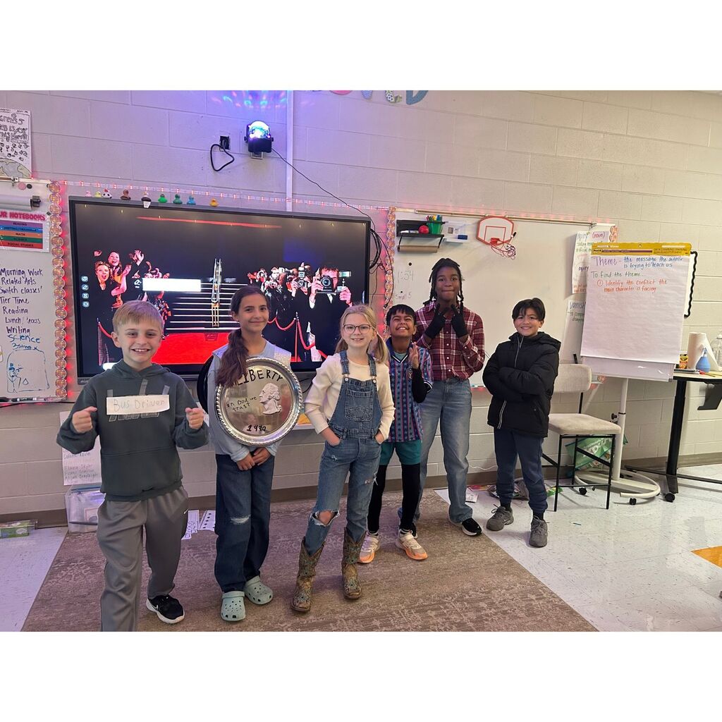 Six elementary students pose in a classroom wearing costumes representing a bus driver, a coin, and other creative characters.