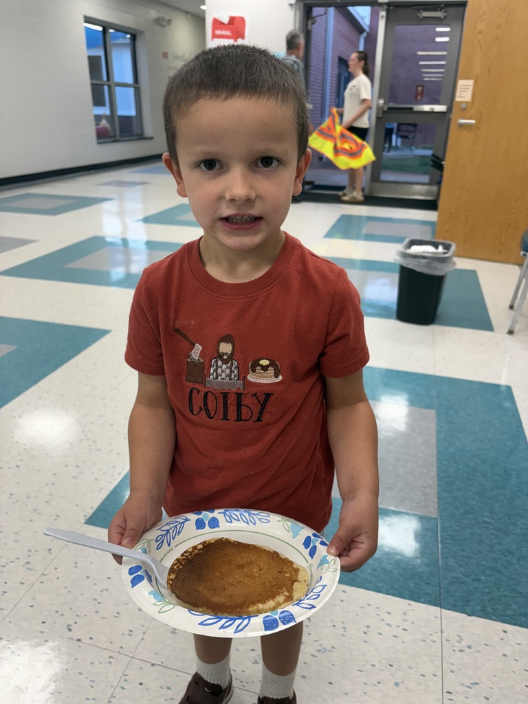A student smiles holding a plate with a pancake on it
