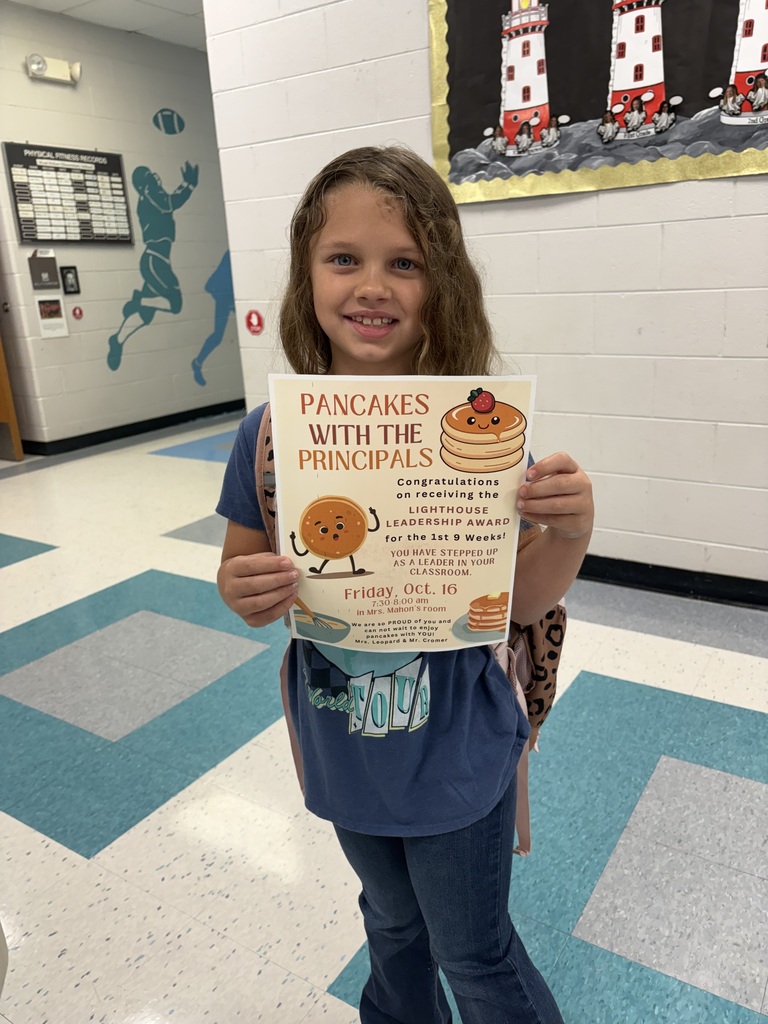 A student smiles holding up a sign about pancakes with principals