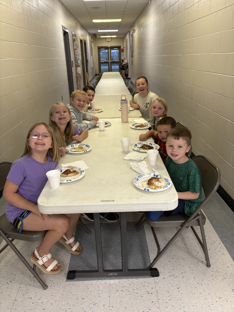 Students sit around a table during the pancake breakfast and smile