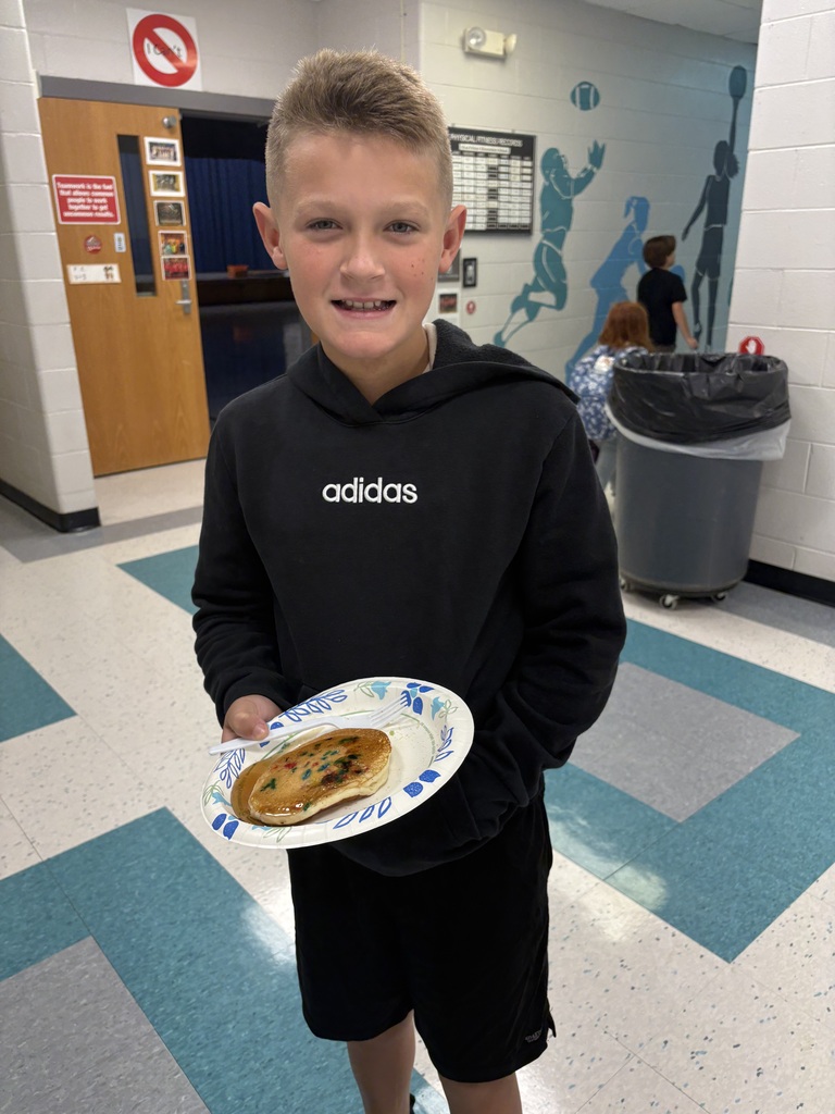 A student smiles holding a plate with a pancake on it