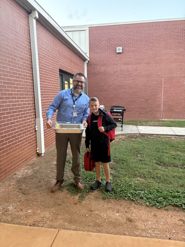 A district leader smiles for a picture with a student while holding a pan of pancakes