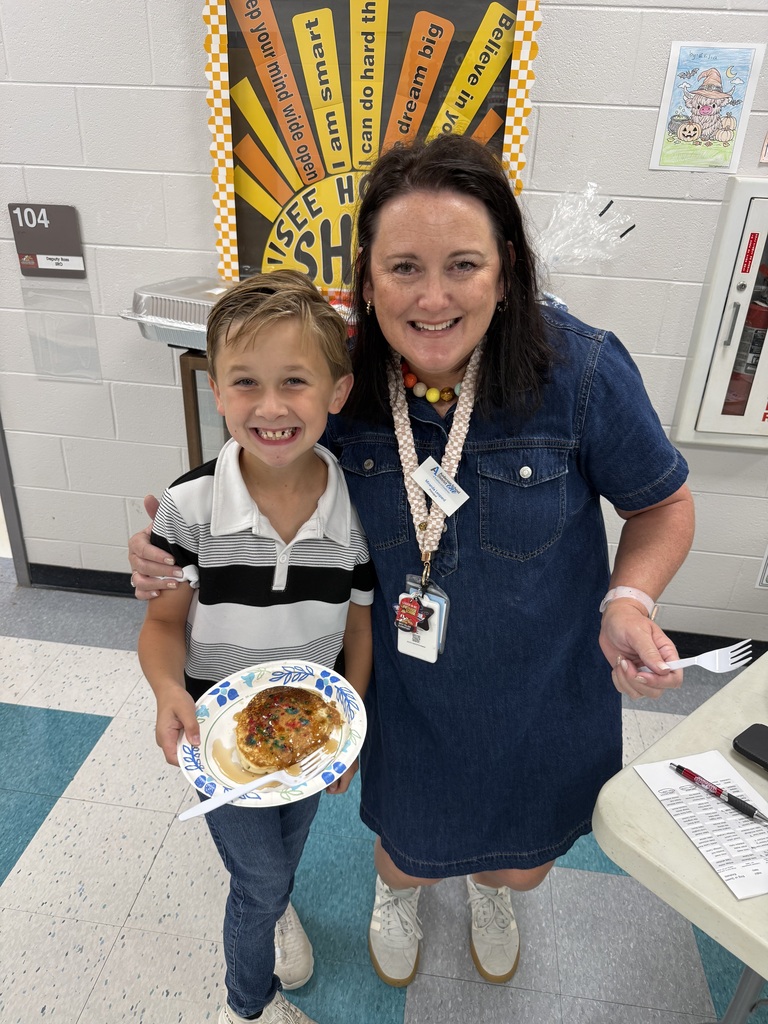 A school leader and student smile while the student holds a pancake