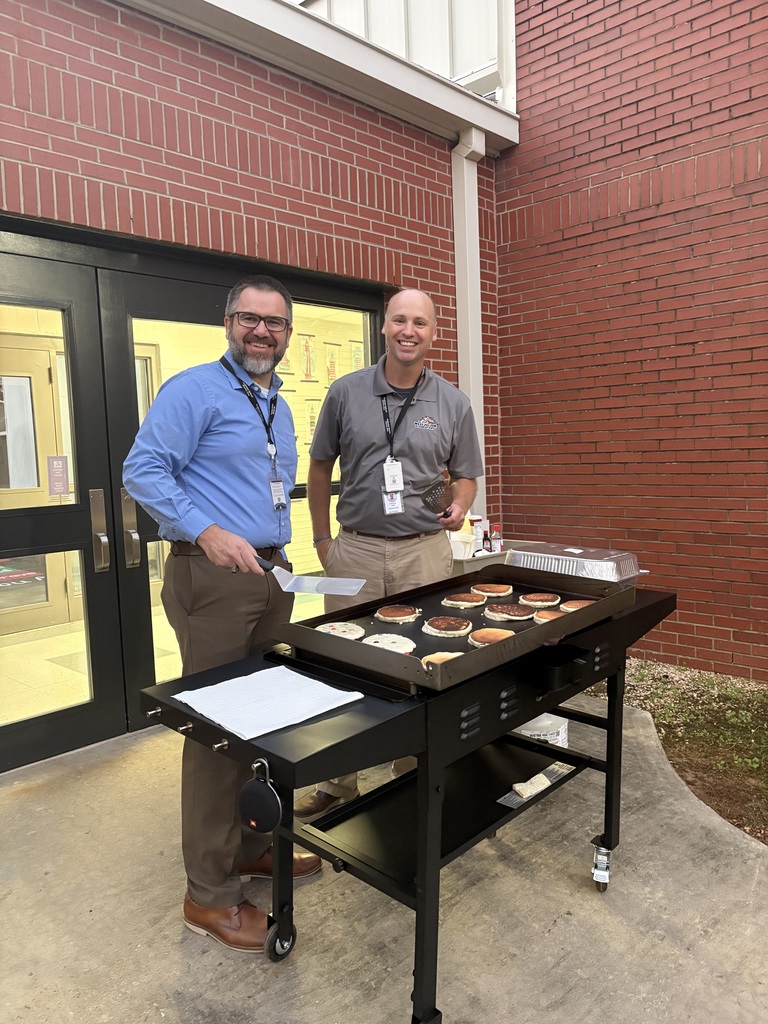 A school leader and district leader stand by the grill and smile while flipping pancakes