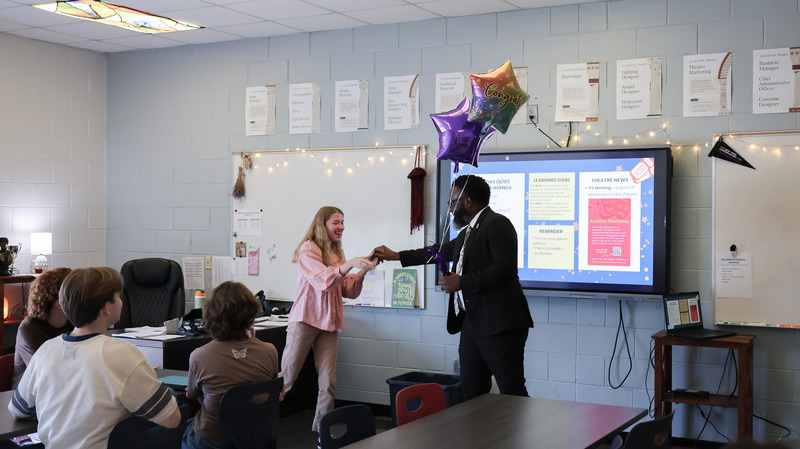 A PTSA representative surprises a staff member with a grant and balloons in her classroom