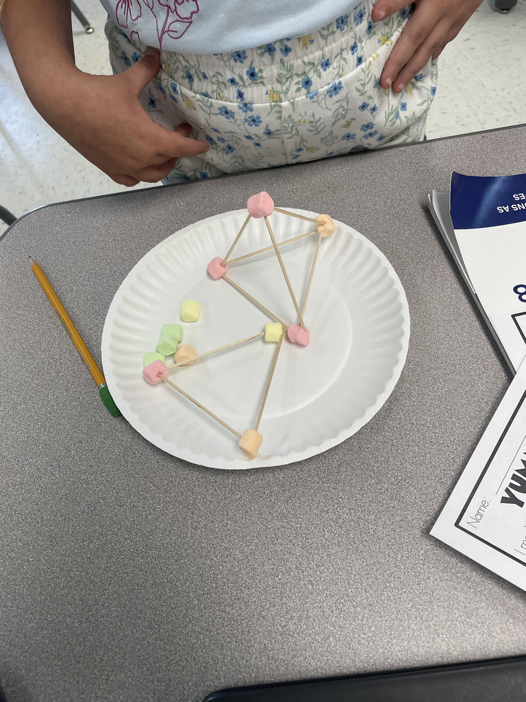 Engineering or snacking? In Mrs. Aaron’s 2nd-grade math class, it’s a bit of both! Our students are moving beyond the textbook to build 2D and 3D shapes from the ground up. By using marshmallows and toothpicks to represent vertices and edges, these young mathematicians are gaining a deeper understanding of geometric properties. Way to go, Grade 2!