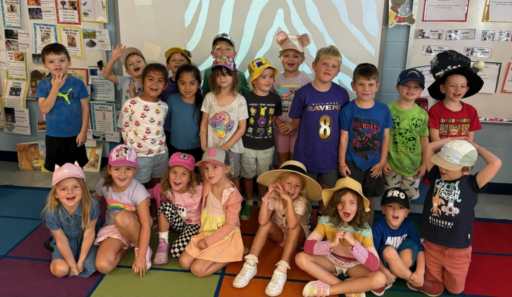 Students standing and seated in front of board in various hats,