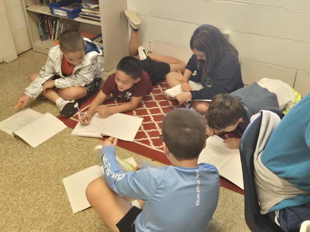 Group of students writing while sitting on an area rug