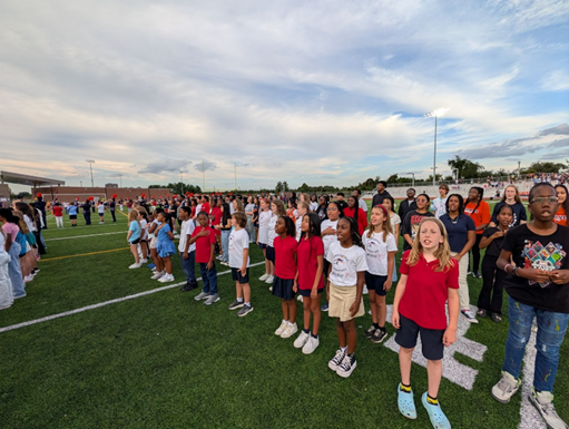 Students singing Star Spangled Banner on football field