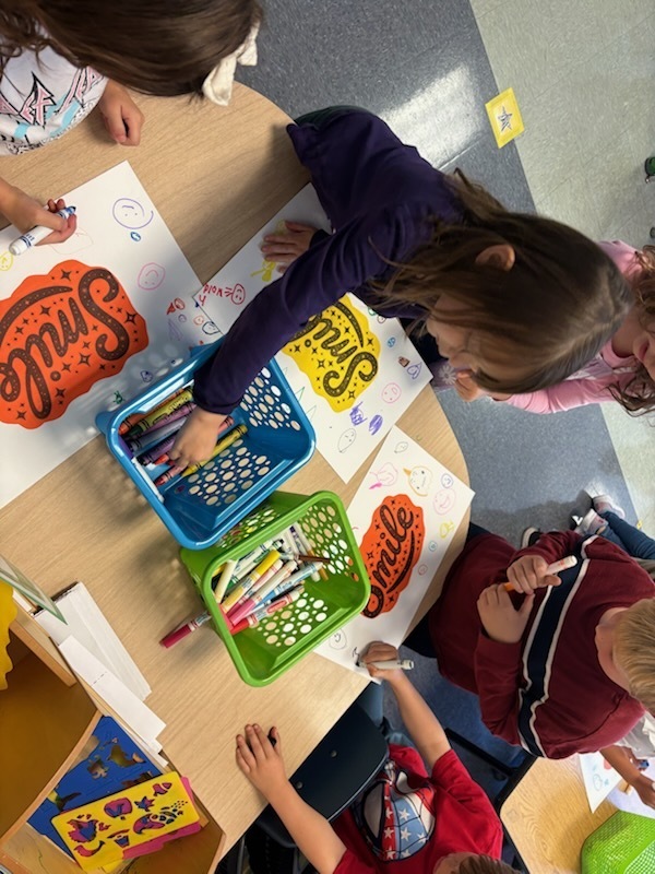 Students coloring posters at a smal table.