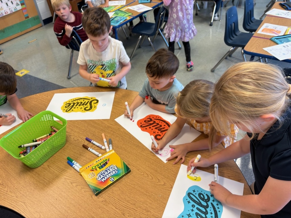 5 students coloring posters at a small table.