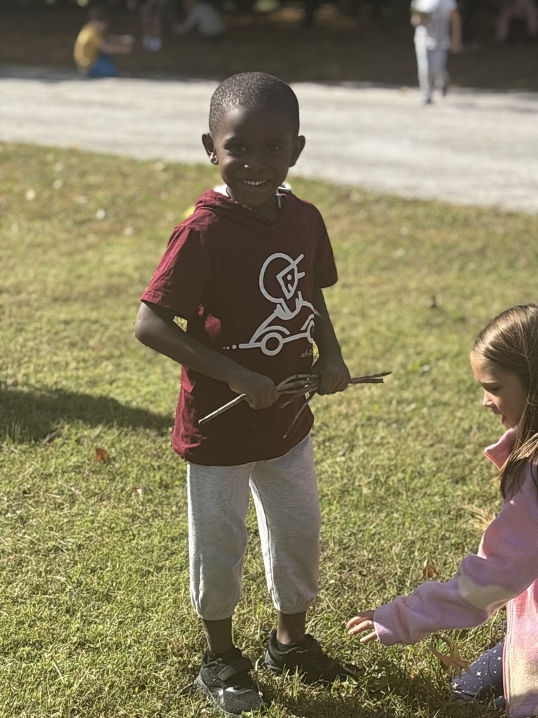 Student smiling holding sticks in his hands outside.