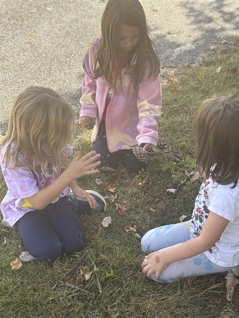 Three students kneeling outside gathering leaves.