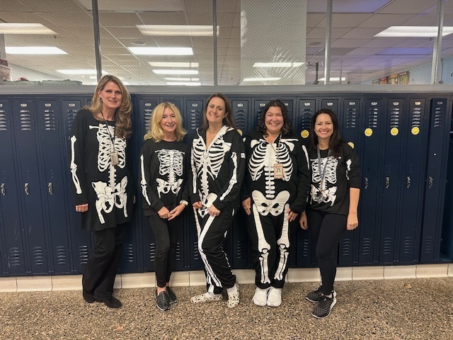 Five women standing near lockers wearing skeleton sweatsuits.