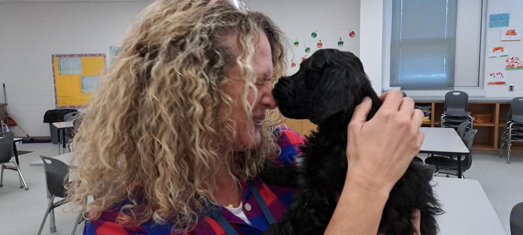 A black puppy giving a teacher a kiss on the nose.