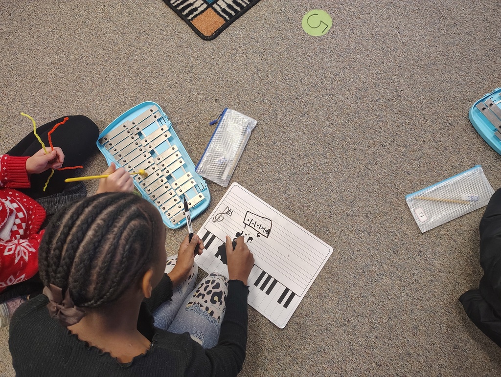 two students with a white board and xylophone working together.