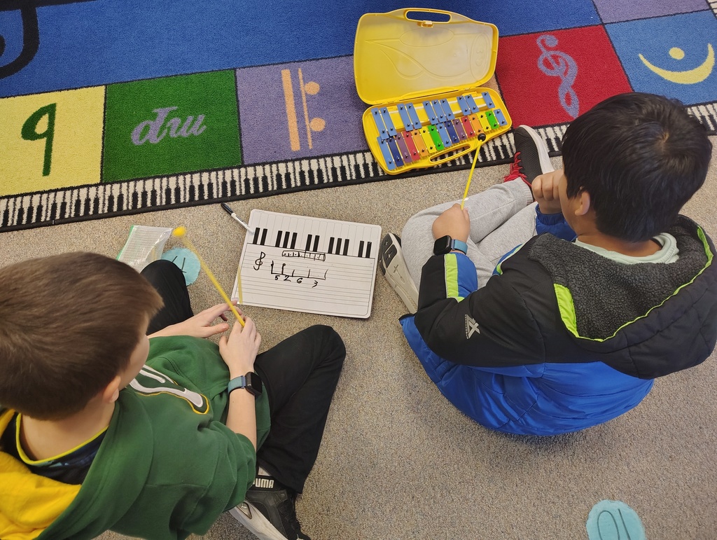 two students with a white board and xylophone working together.