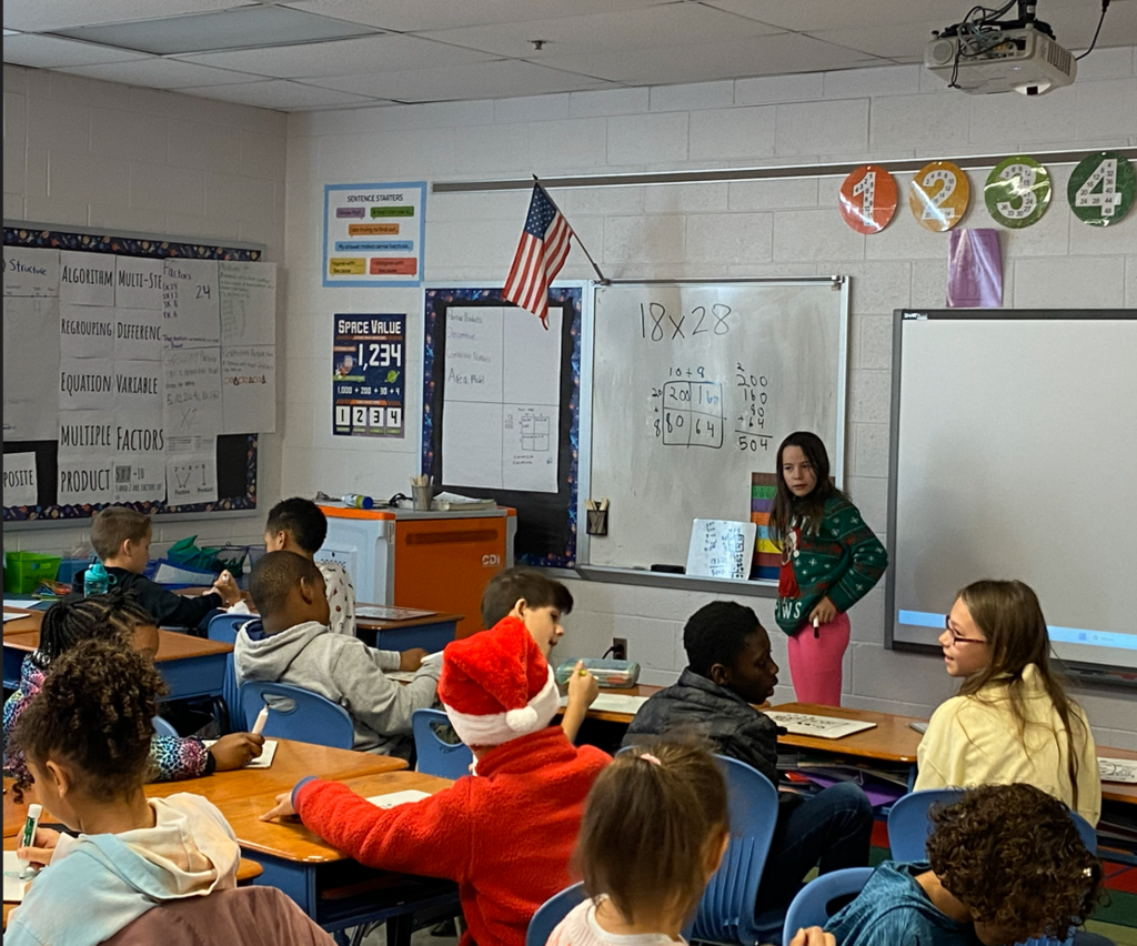 Student standing at whiteboard explaining her math problem solving