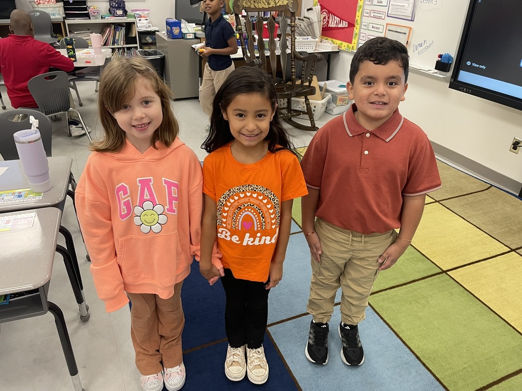 Three students standing and smiling, wearing orange.