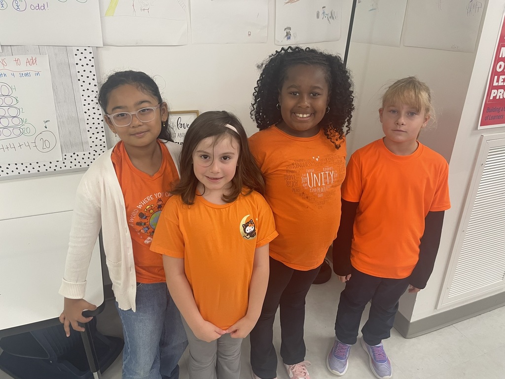 Four students standing and wearing orange, smiling