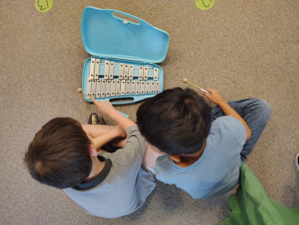 Students sitting and playing a silver and blue glockenspiel