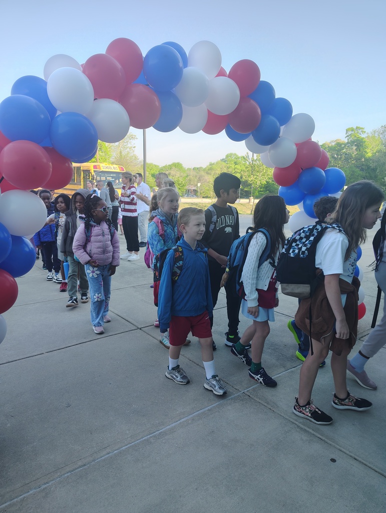 red, white, and blue balloon arch, students walking under it to enter school