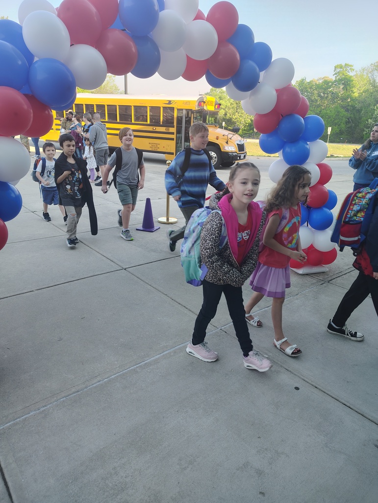 red, white, and blue balloon arch, students walking under it to enter school