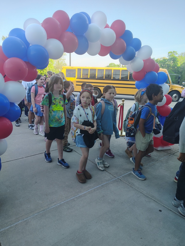 red, white, and blue balloon arch, students walking under it to enter school