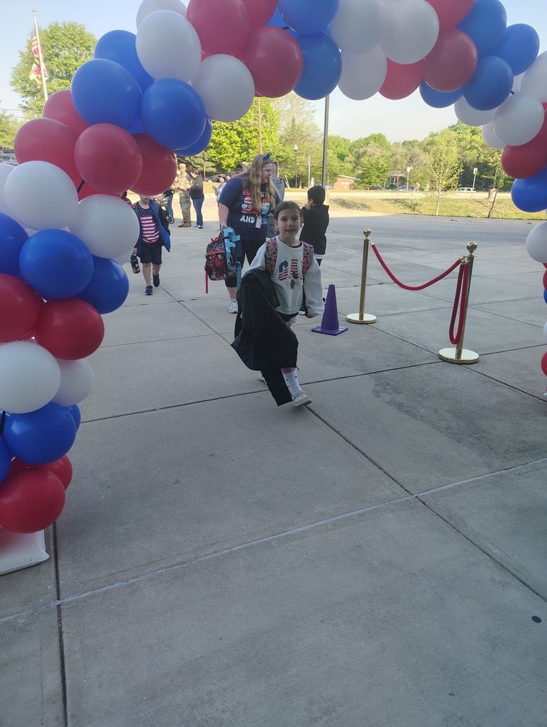 red, white, and blue balloon arch, students walking under it to enter school
