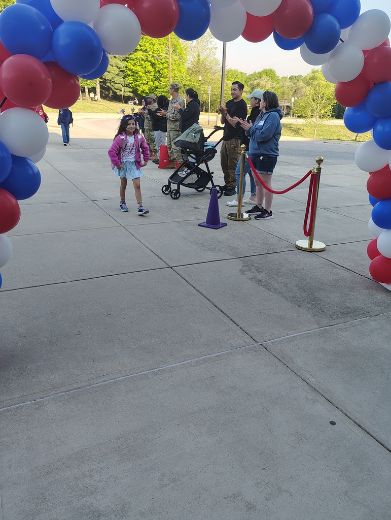 red, white, and blue balloon arch, students walking under it to enter school