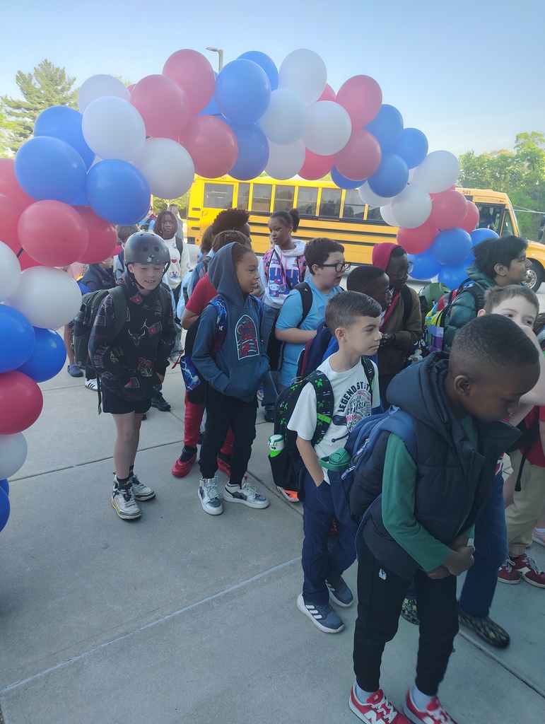 red, white, and blue balloon arch, students walking under it to enter school