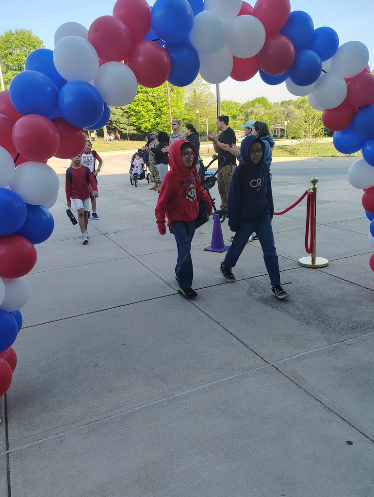 red, white, and blue balloon arch, students walking under it to enter school