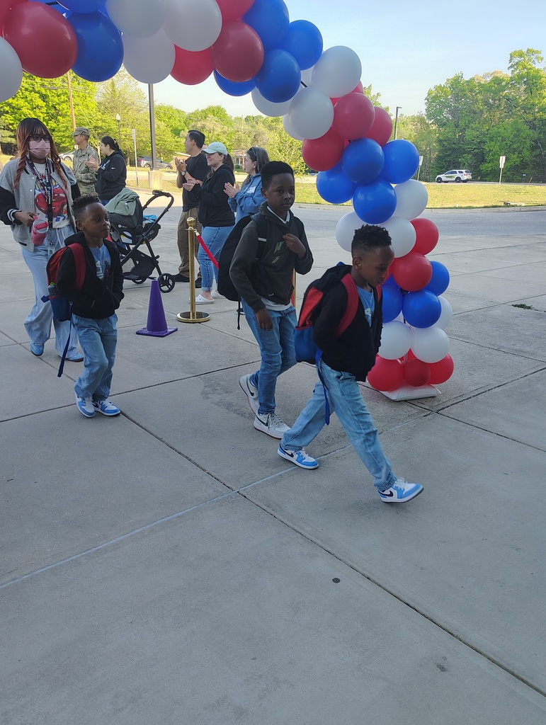 red, white, and blue balloon arch, students walking under it to enter school