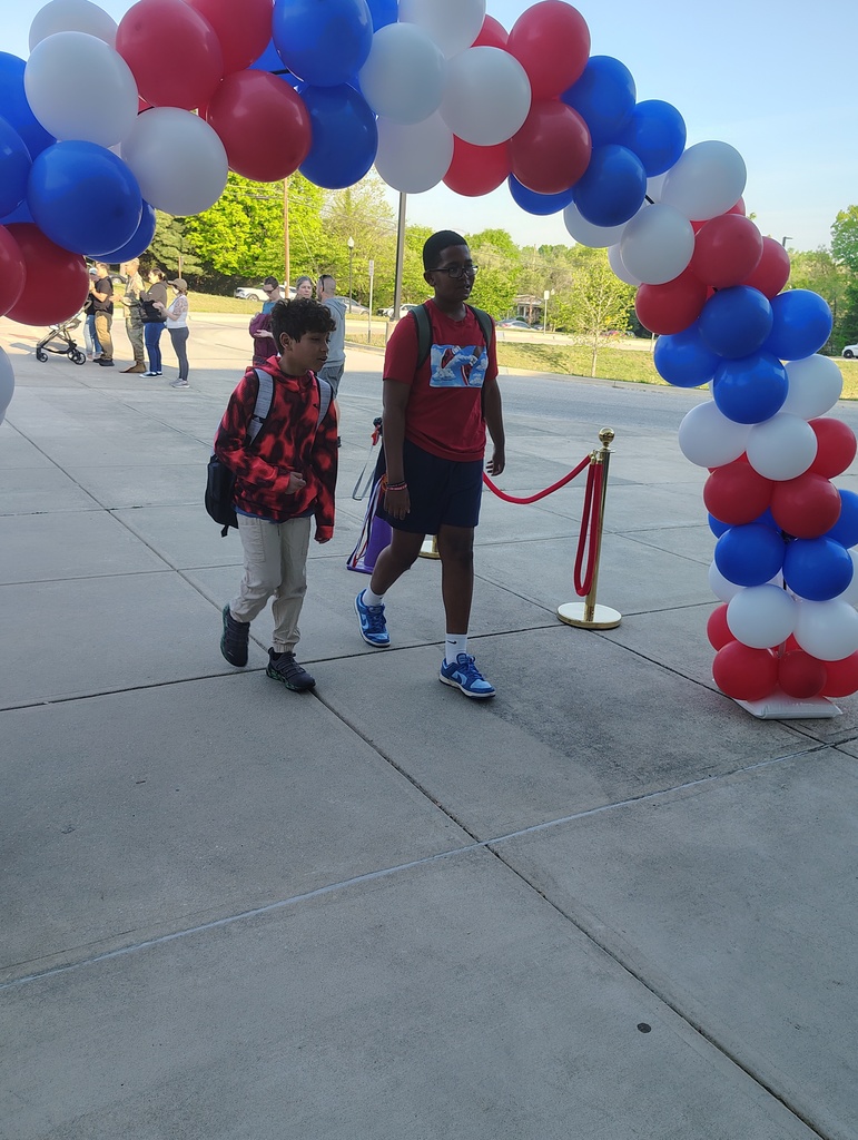 red, white, and blue balloon arch, students walking under it to enter school