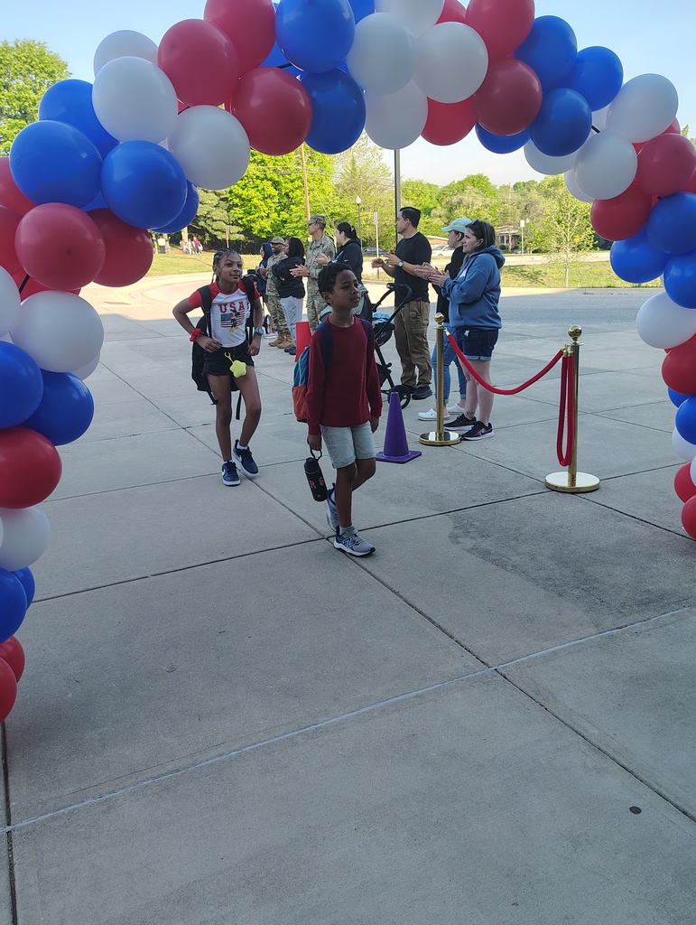 red, white, and blue balloon arch, students walking under it to enter school