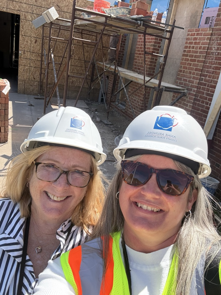 Principal Hamlin and Principal secretary Chris Ritz wearing hard hats smiling in front of Carver EEC under construction