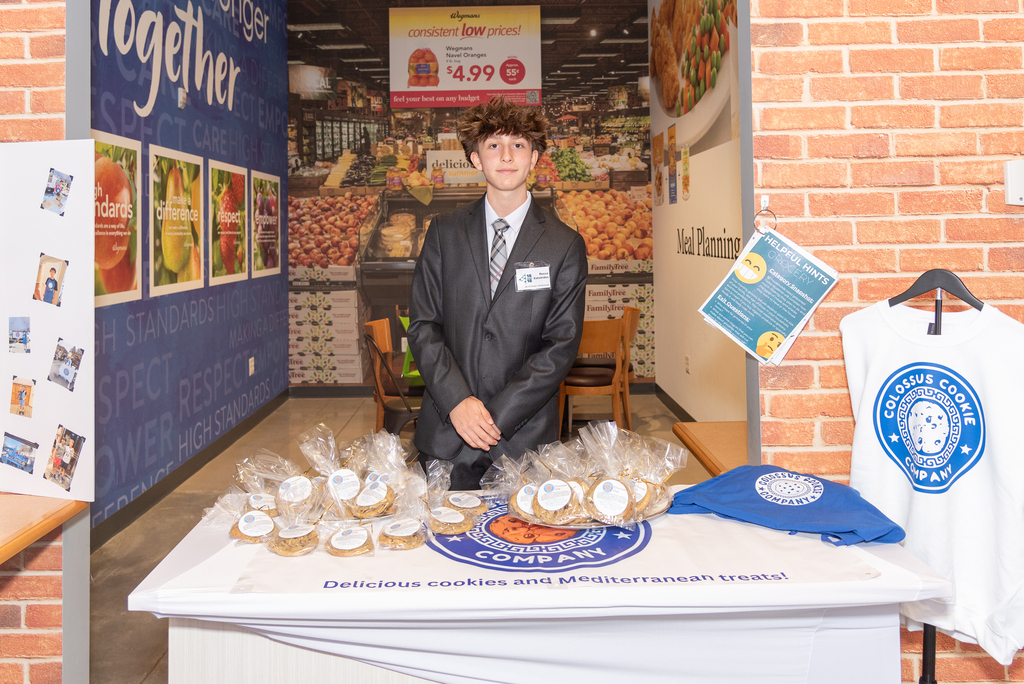 Rocco stands behind a table with cookies and a blue bag, in front of a brick wall.