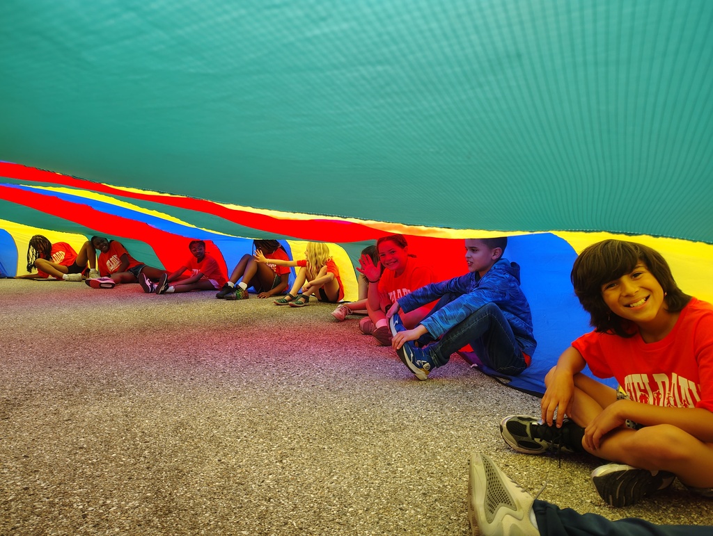 students sitting on the ground under a parachute