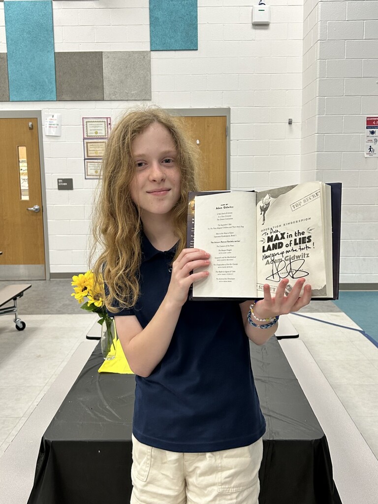 A girl in a blue shirt and white pants holds an open book with the title "The Land of Lies".