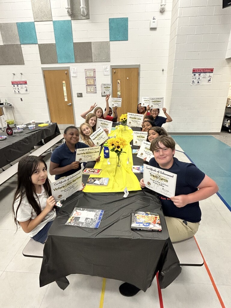 A group of students pose with certificates at a table in a room. The table is covered in black cloth.