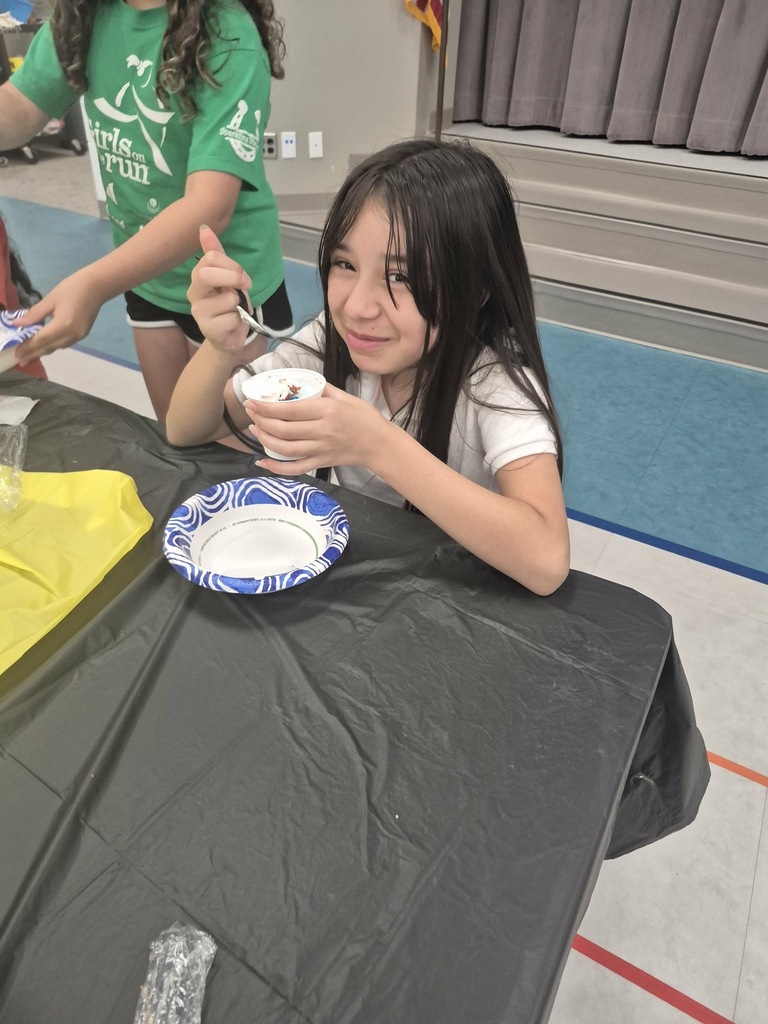 A girl in a white shirt sits at a table with a dessert on a plate, another girl nearby.