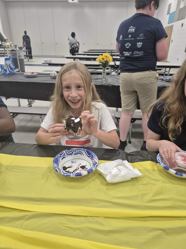Girl sitting at a table with a dessert, smiling. Two more people sitting behind her.