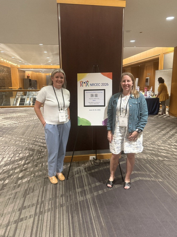 two women standing in front of conference sign smiling