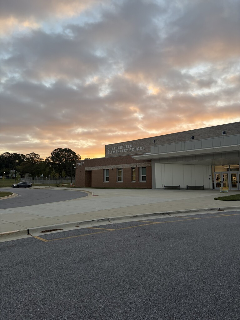 A building with a parking lot in front. A car is parked. A sunset sky with clouds.