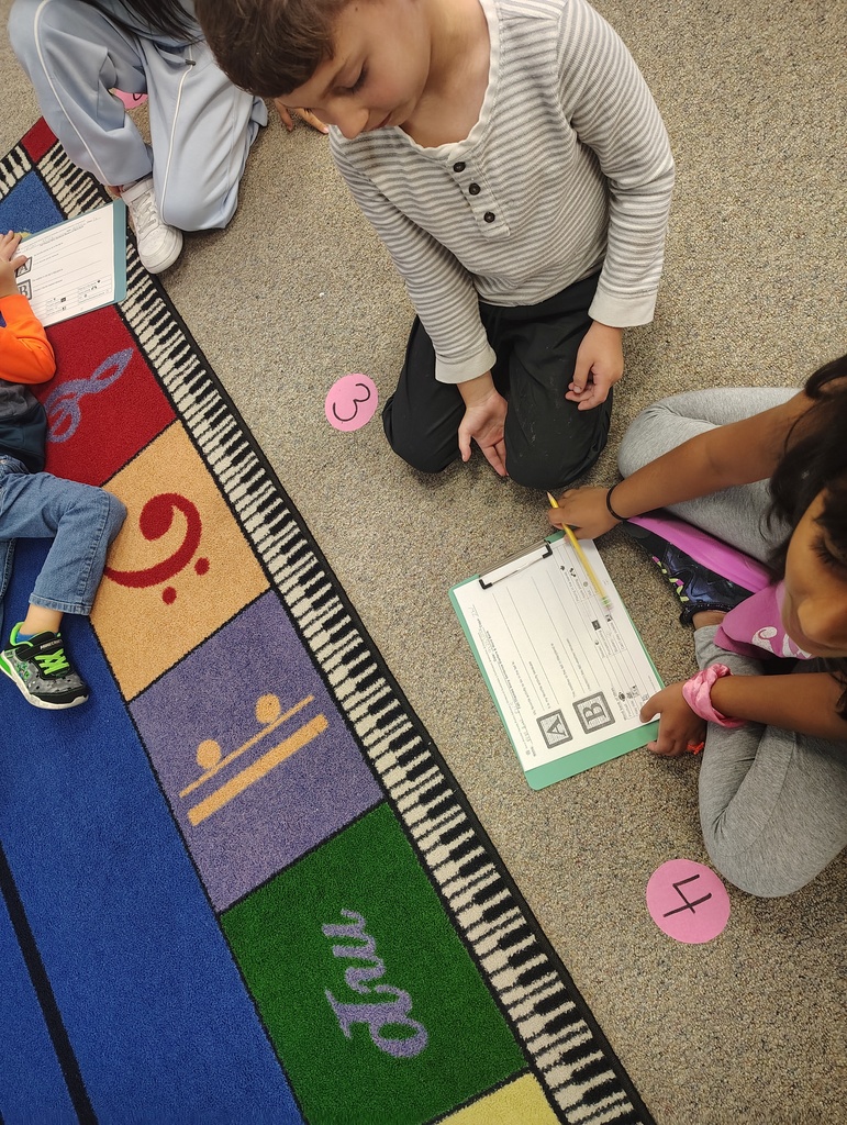Two children, one holding a pencil, sit on a rug with a piano-key rug and pink numbers.